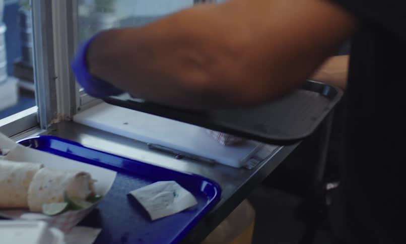 An employee prepares a meal in a food truck as people wait or walk by