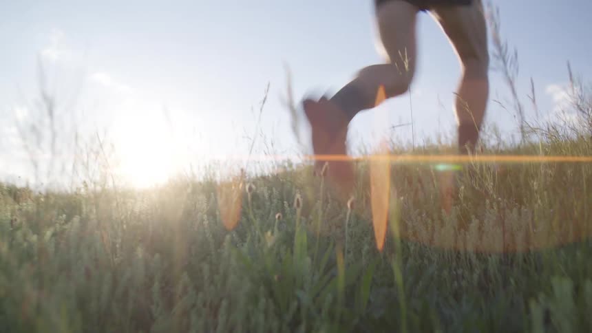 Legs of a person running on grass during the day