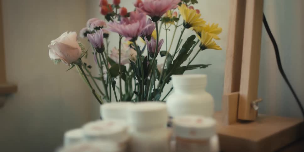 A wooden bedside table with bottles of pills a wooden lamp and a flower vase