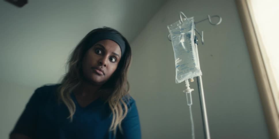 A nurse looks up from writing in a folder and checks an iv bag after looking concerned