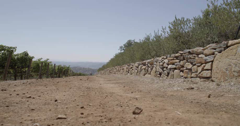 Dirt road with a cobblestone type wall leading toward some mountains