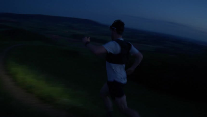A man wearing a headlamp runs down a dirt trail at night