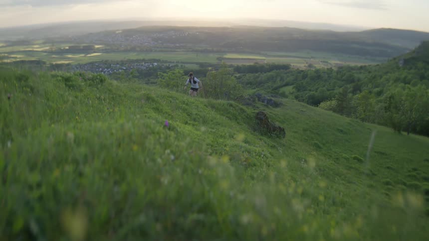 A young man runs up a hill near a rural community sitting in a valley