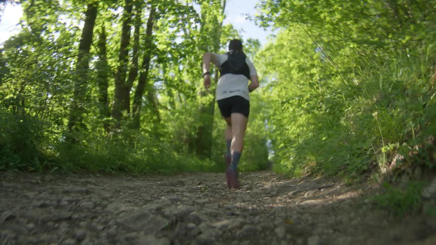 Runner from behind jogging on a dirt path through a lush green forest