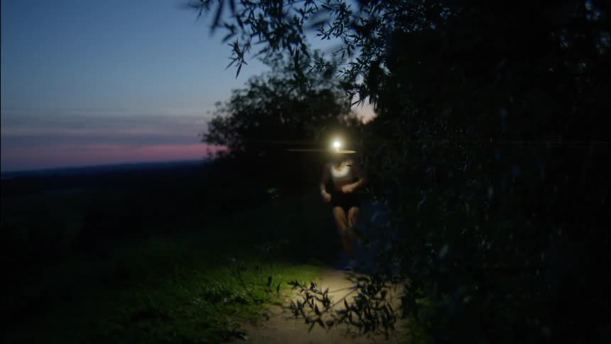 Runner wearing a headlamp jogging along a trail at dusk