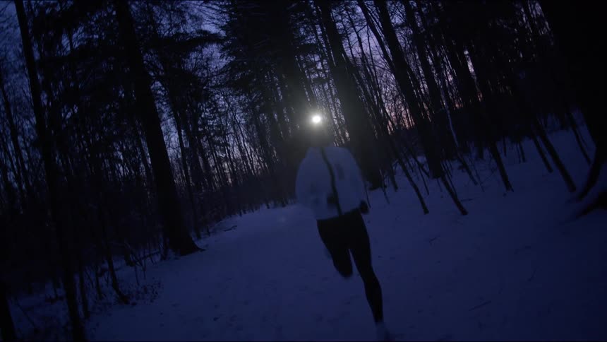 A woman jogging across a snowy forest with a lantern on her head
