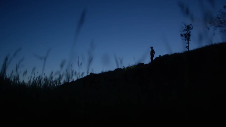 Silhouette of a person with a headlamp on a hill in a dark dawn sky