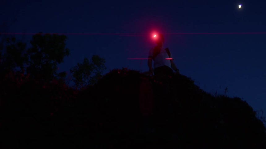 Man wearing a red headlamp stands on a promontory at night and looks around