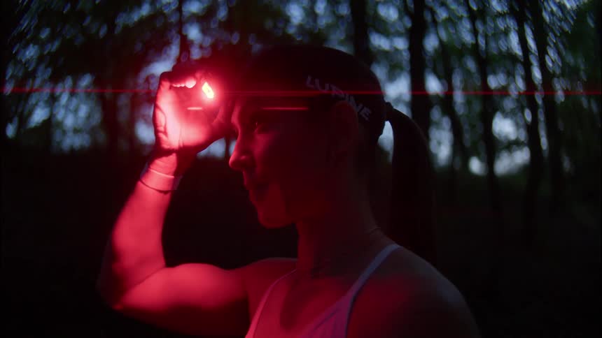Woman in a dark forest turning off the flashlight with red light that is on her head