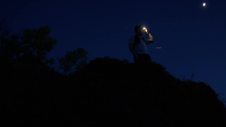 Man standing on a promontory at night adjusts the color of his headlamp as he looks around
