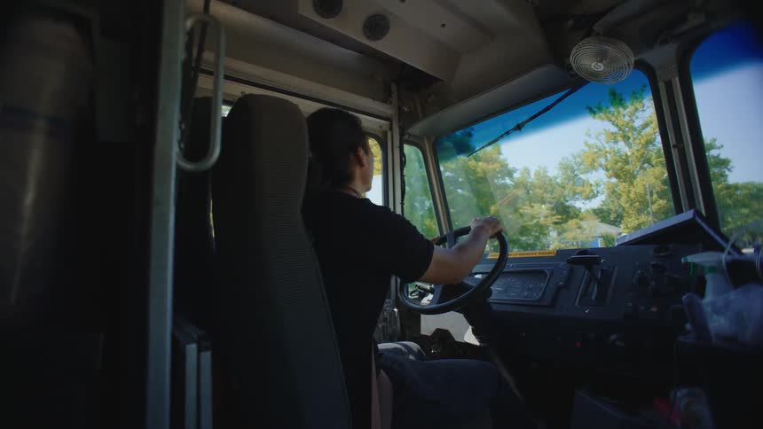 A man is sitting and driving a large vehicle and turning the steering wheel