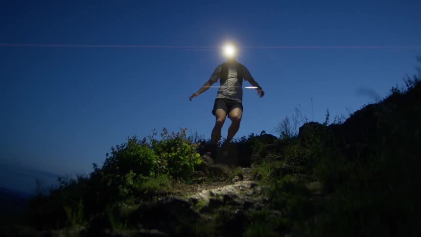 A person is going down a hill wearing a helmet with a lamp at night