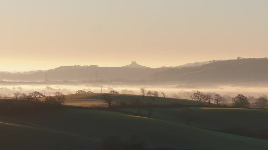 Fog hangs over a body of water in between hills and grass plains