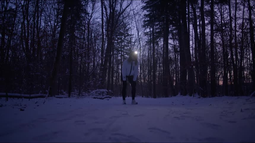 Woman breathing and walking in a snowy forest with trees around and a purple sky day