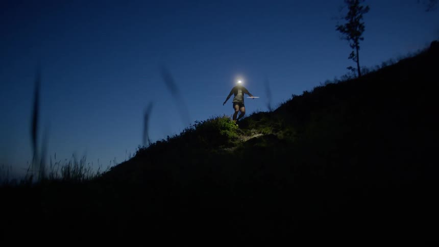 Male runner wearing a headlamp runs down a grass covered slope at night