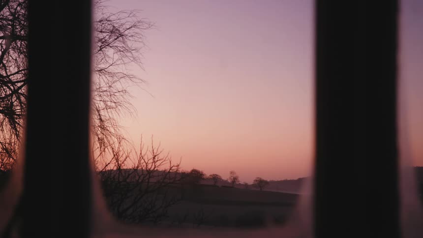 View from a window to a field with hills on a day with a purple sky