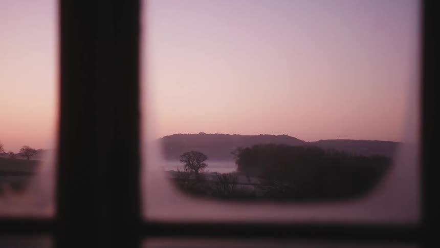 A window with condensation on it reveals a lake and mountain scene outdoors
