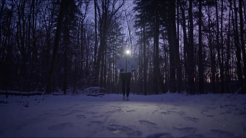 A person running through a forest at dusk with a light on their head stops to take a breather