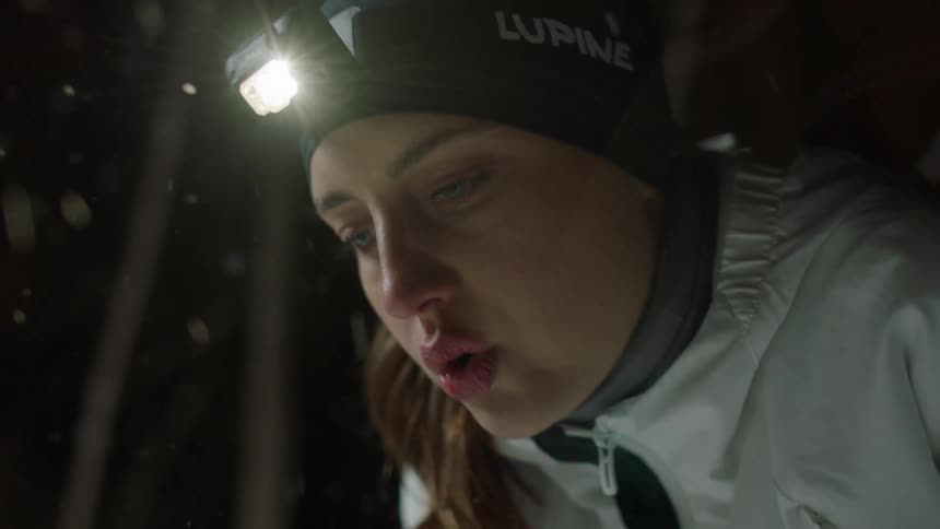 Portrait of a woman with a flashlight on her head taking a deep breath while standing in a snowy forest at night
