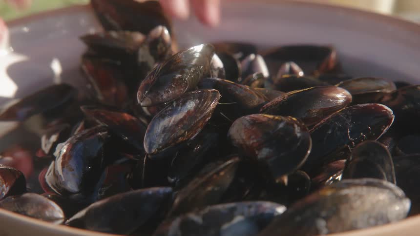 A person grabs clams from a bowl after being cleaned