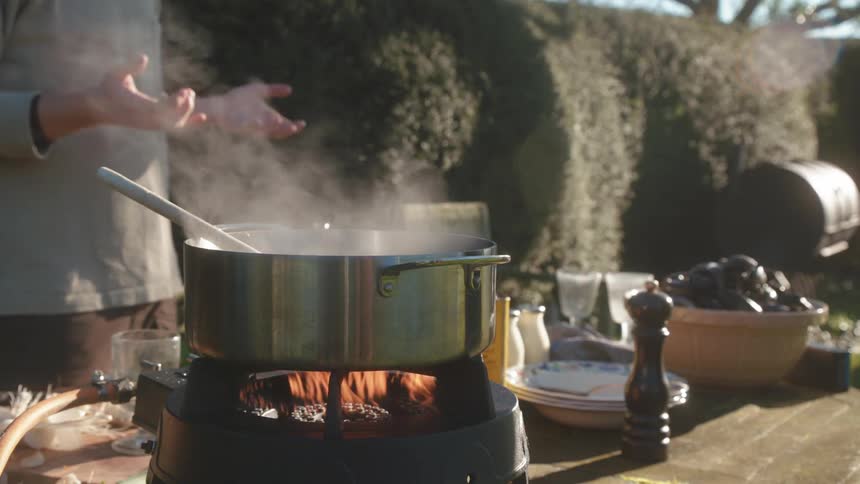 Two people outside talking while a pan cooks over a portable oven