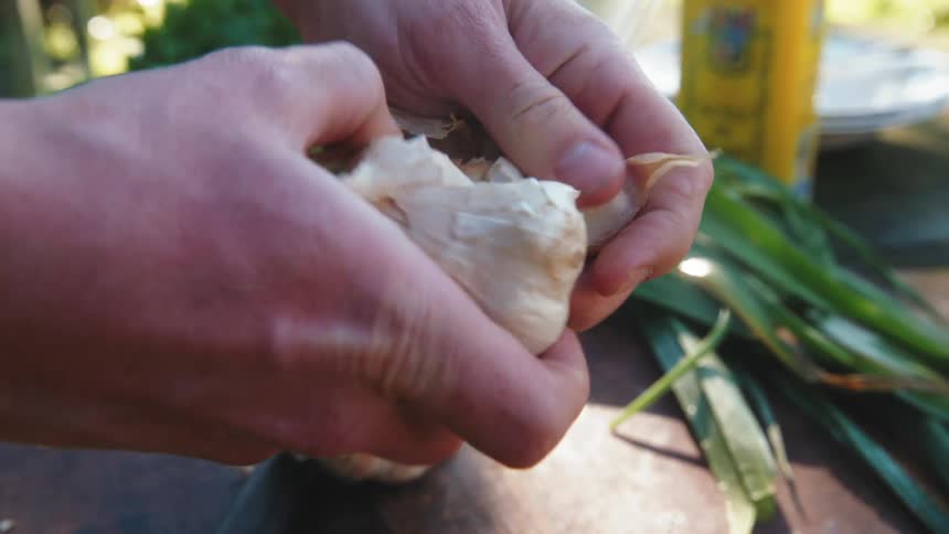 A man pulls a garlic bulb apart on a table outdoors