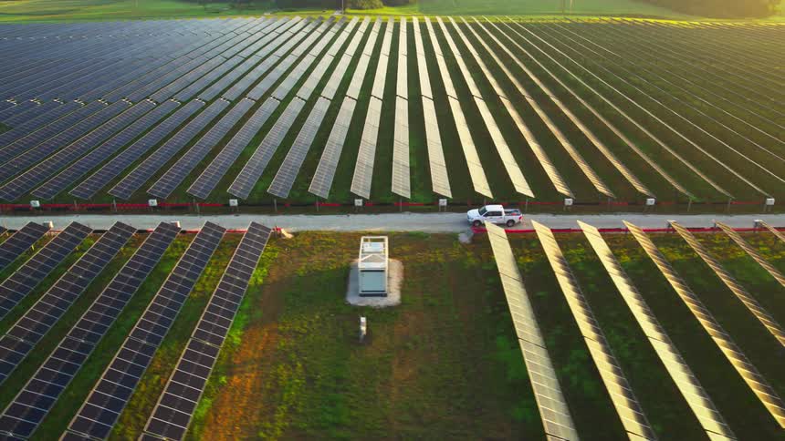Expansive solar farm with rows of panels and a white truck driving through