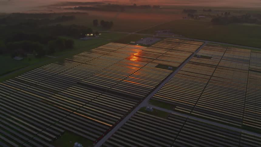 Panorama of solar panels on an agricultural field at reddish sunrise on the horizon