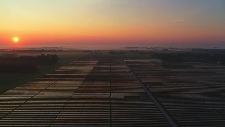 Aerial panorama with the reddish sunrise on the horizon and a field full of solar panels