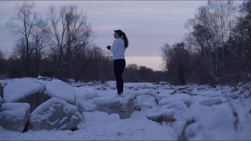 Woman runs across a snowcovered field at dawn with bare trees in the background