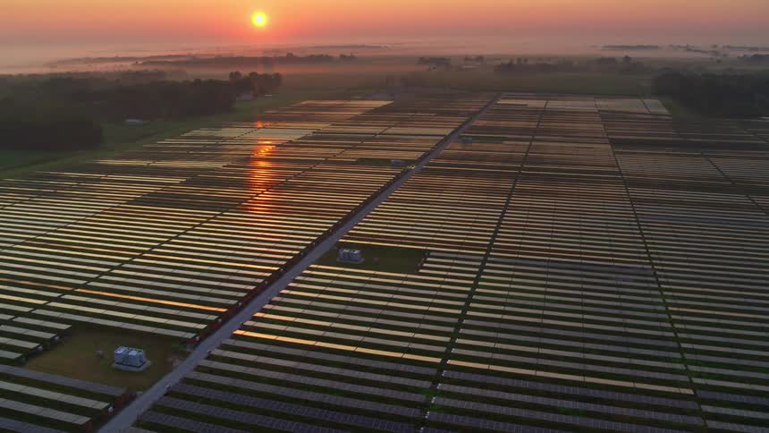 Aerial view of solar panels with an orange sun on the horizon