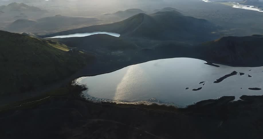 Aerial view of a lake reflecting sunlight surrounded by a mountainous landscape