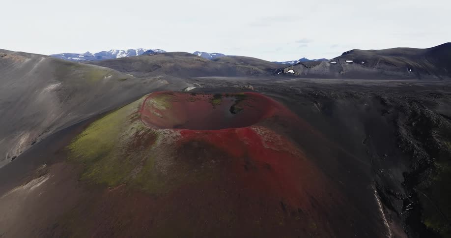 A volcano covered in moss at the top in front of mountains