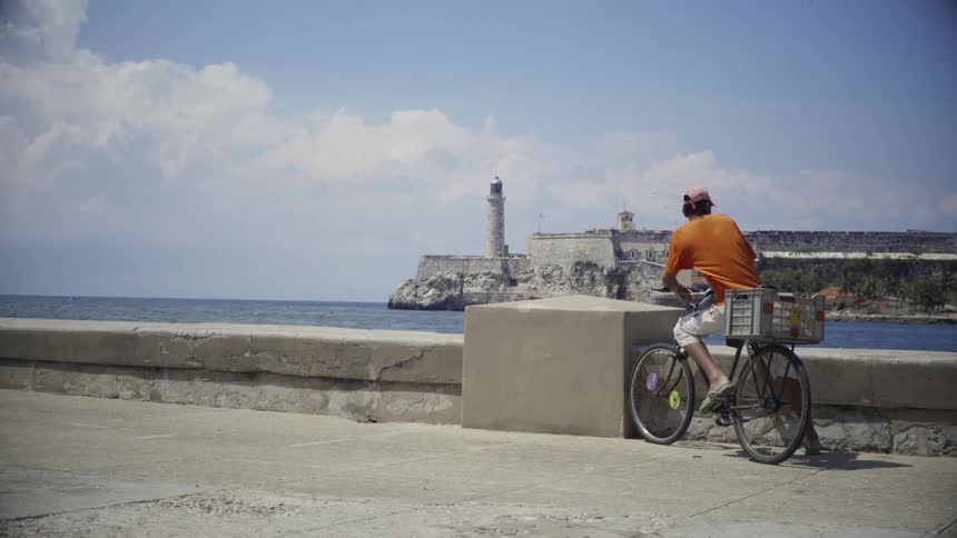 A guy sitting on a bike staring at a lighthouse