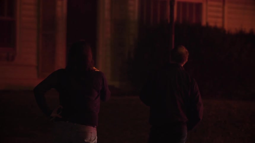 A man and woman stand outside a house that is on fire at night