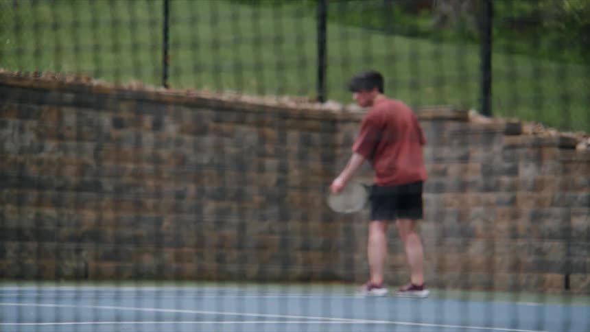 A man in a red shirt is hitting a tennis ball using a racket on a tennis court
