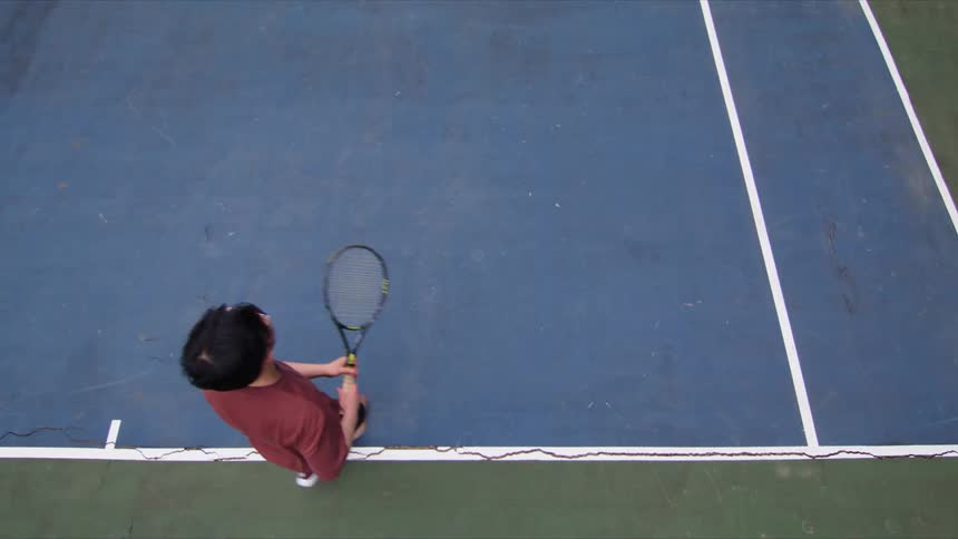 An asian man plays tennis on an outdoor court