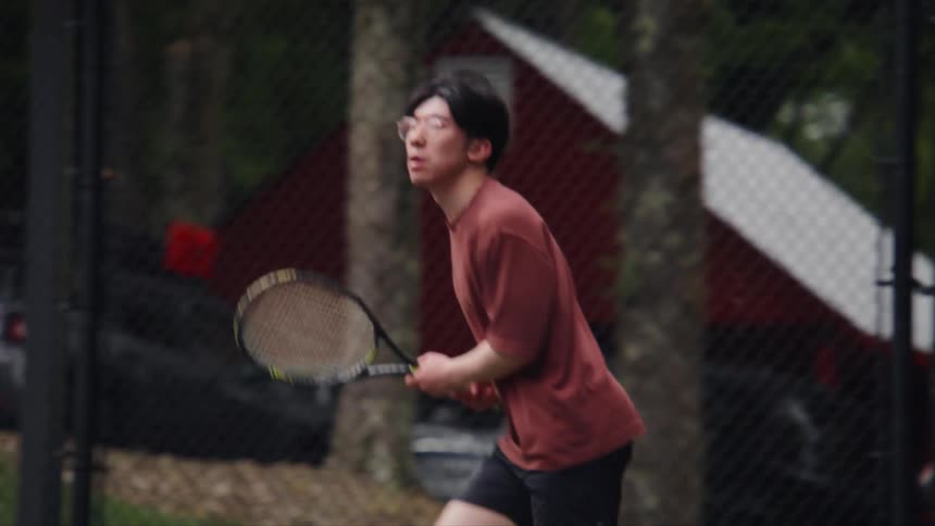 An asian man laughs after playing tennis on an outdoor court
