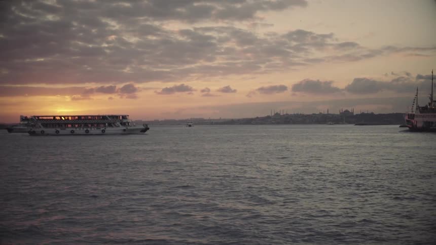 A large ferry passes in the water at sunset
