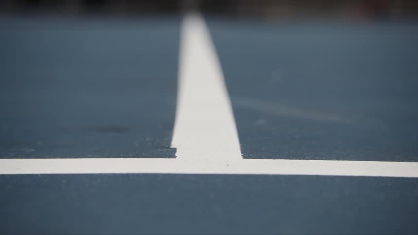 A tennis ball rolls back and forth over white tennis court lines