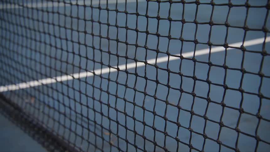 A man grabs a tennis racquet leaning against a net on a court