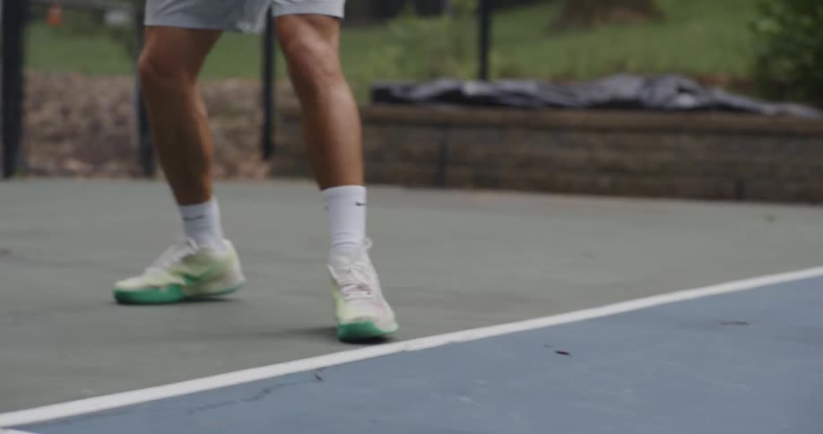 A young man plays tennis on a court in a park