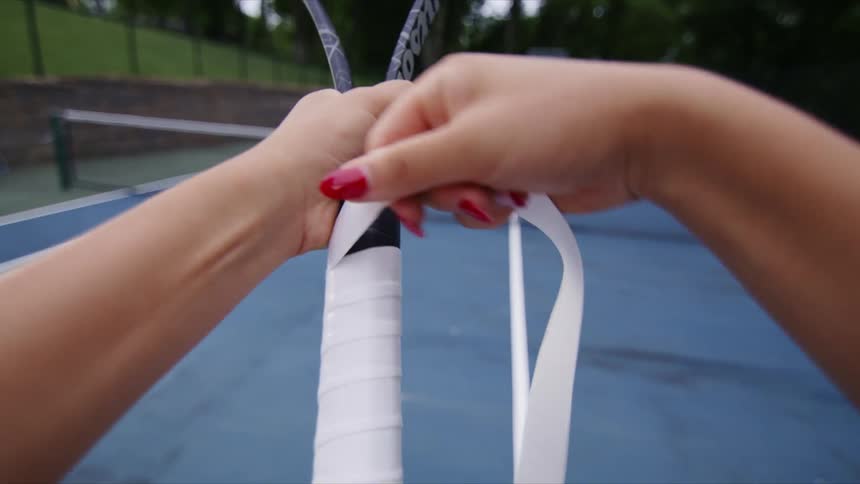Female hands with red nails wrapping a white ribbon around a tennis racket