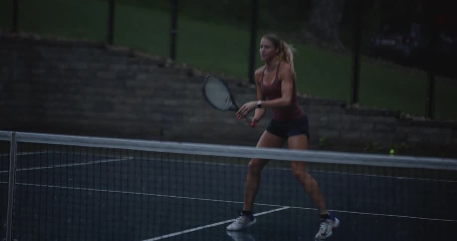 Woman playing tennis on a court on a rainy day