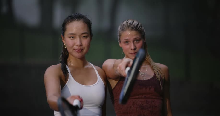 Two young women holding tennis rackets burst out laughing