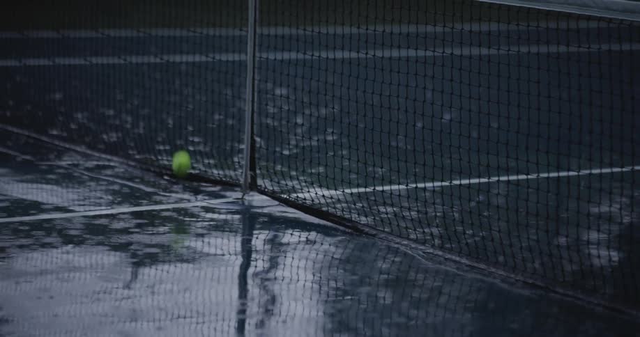 Green tennis ball hitting the net on a rainy court