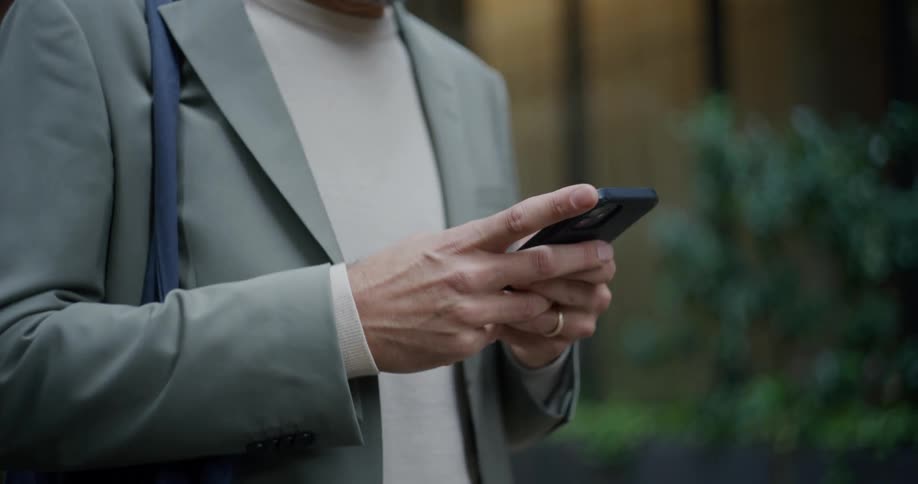 A man standing outside a city building starts texting on a phone
