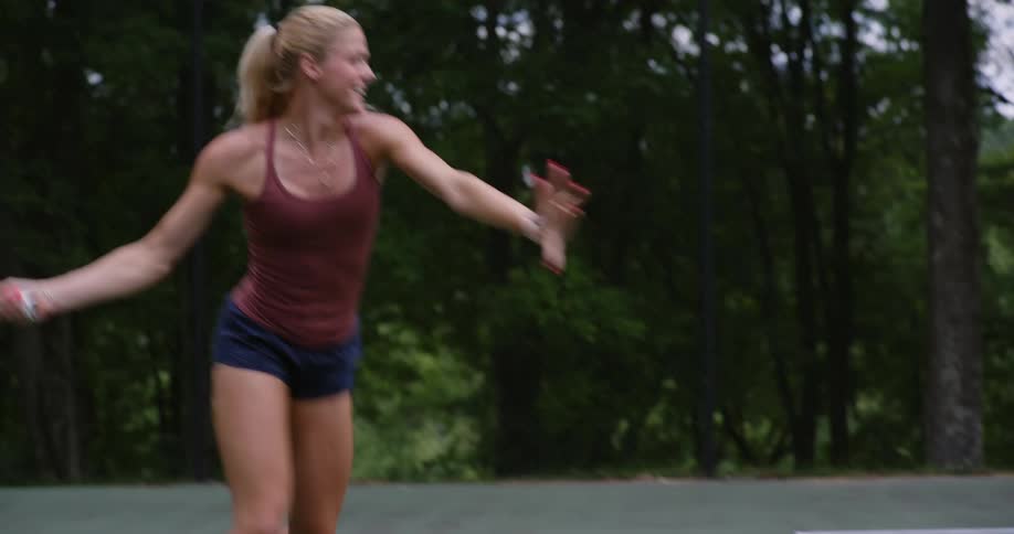 Excited blonde woman playing tennis on an open court