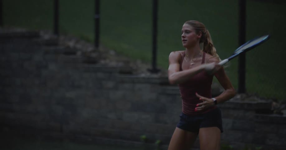 A young fit woman playing tennis on a court while raining
