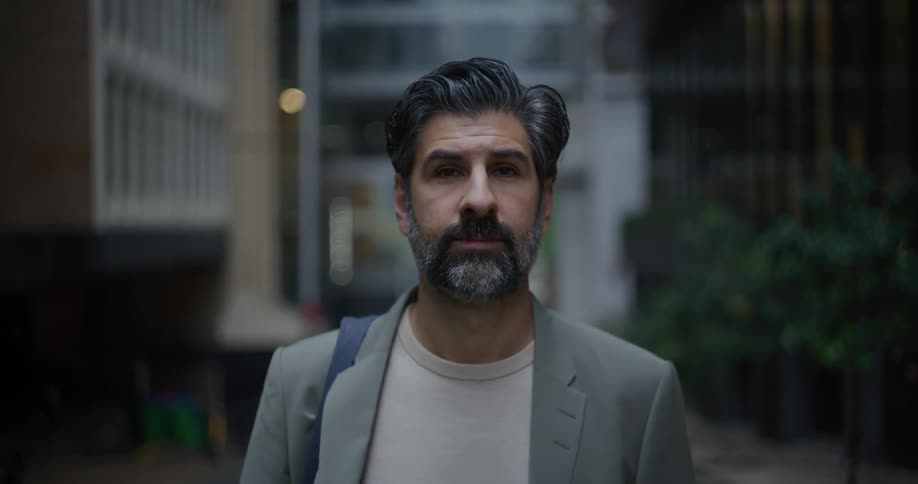 A man with a partially gray beard and wearing a gray blazer is staring straight ahead
